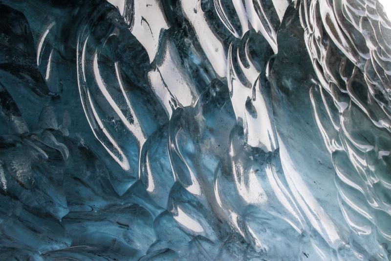 Deeply ridged, wave-like folds in blue glacier ice, catching bright light from one side