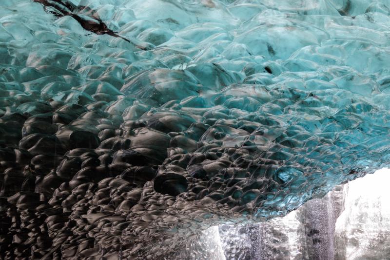 The underside of a glacier ceiling, its surface of small rounded ridges fading from pale teal ice to near black