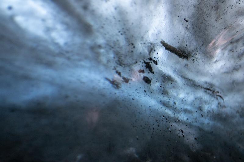 Macro close-up of glacier ice embedded with dark volcanic grit and sediment, softly out of focus
