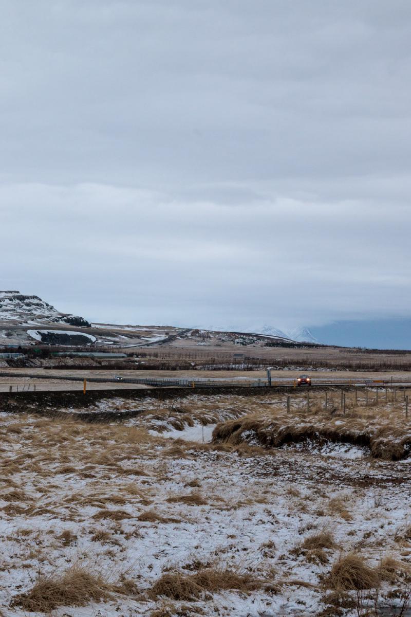 A car driving along a coastal road through a wide, snowy valley with mountains in the distance