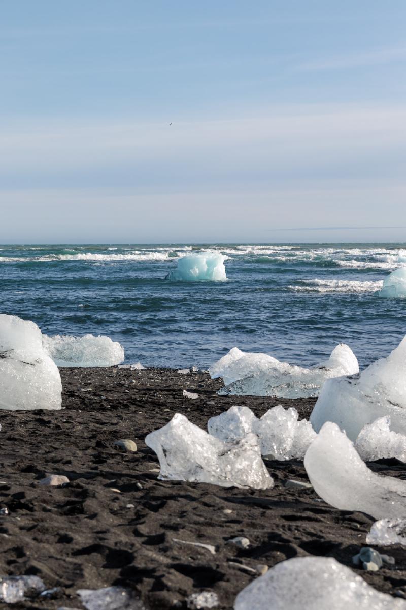 Chunks of glacier ice scattered on a black sand beach, with ocean waves breaking behind them